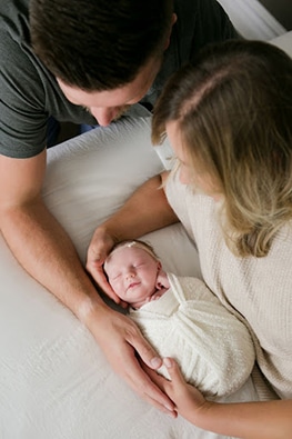 swaddled newborn within parents arms