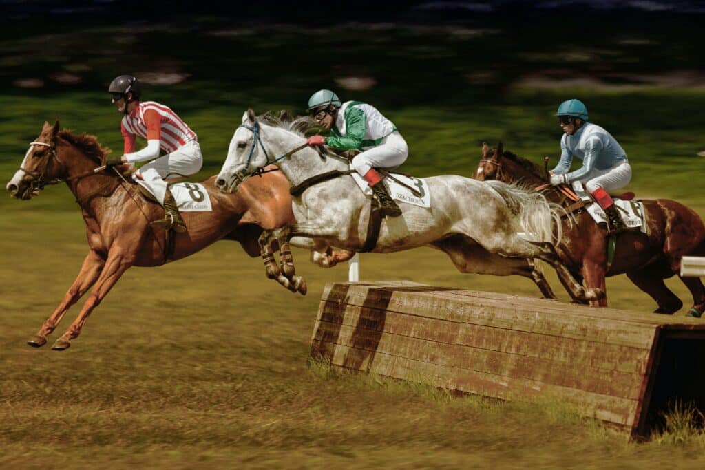 three riders and horses making a jump during a race at the San Siro hippodrome in Milan