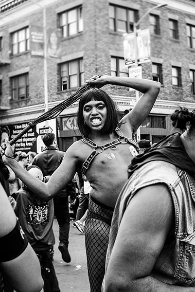 LGBTQIA person in a crowd, wearing a harness and fishnet tights.