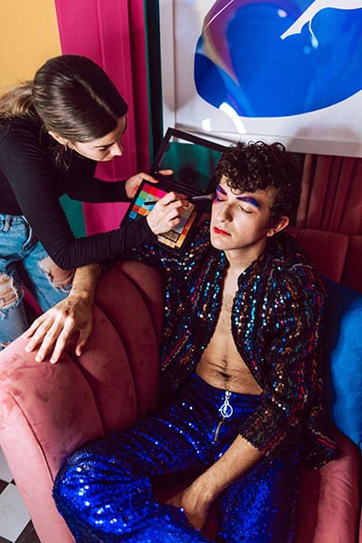 makeup artist applying colorful makeup to person in sequined clothing