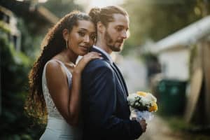 bride leaning the front of her body into the groom's back, her hand resting on his shoulder while the groom holds the bouquet