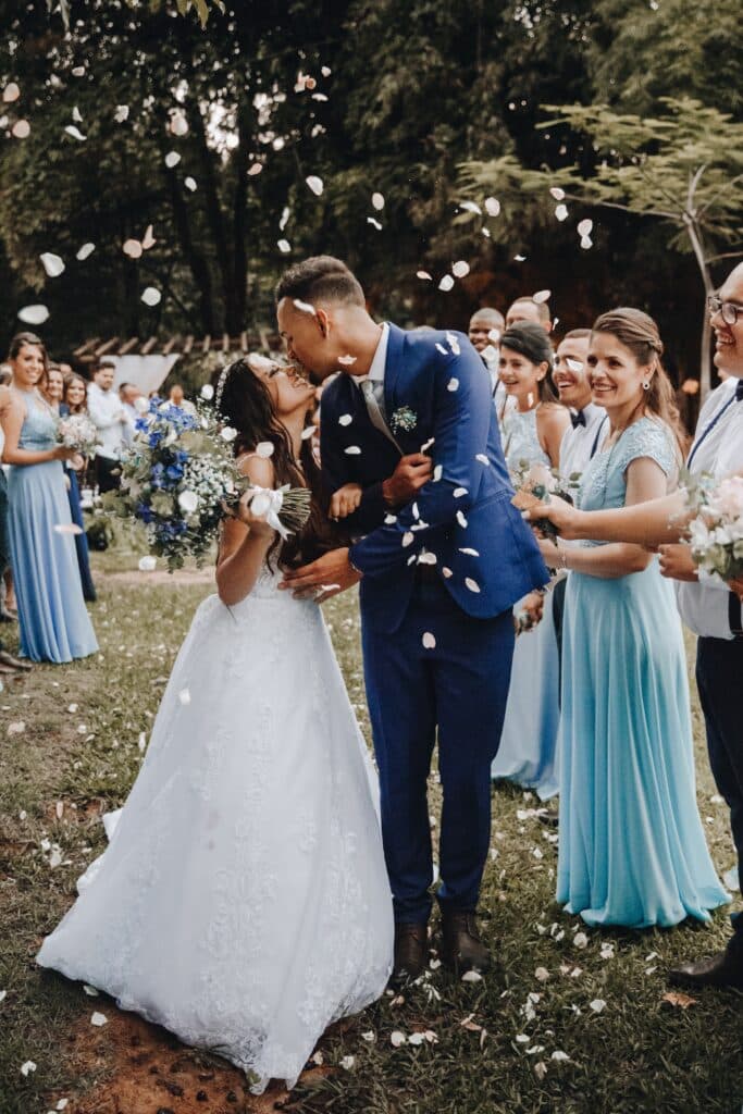 bride and groom kissing while walking down aisle being showered with white flower petals