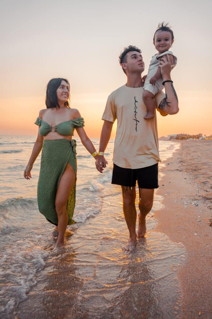 couple holding hands while dad carries toddler at the beach