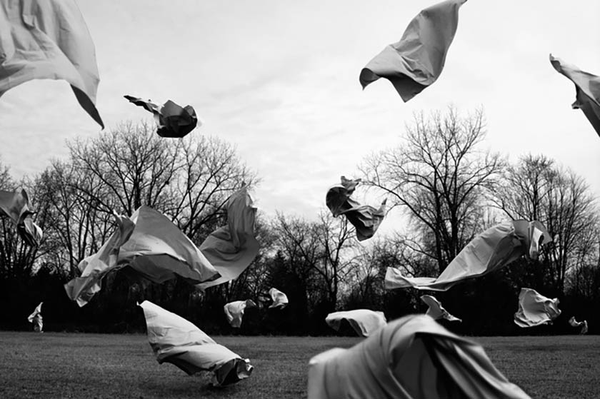 scraps of fabric blowing in the air throughout a tree-lined field