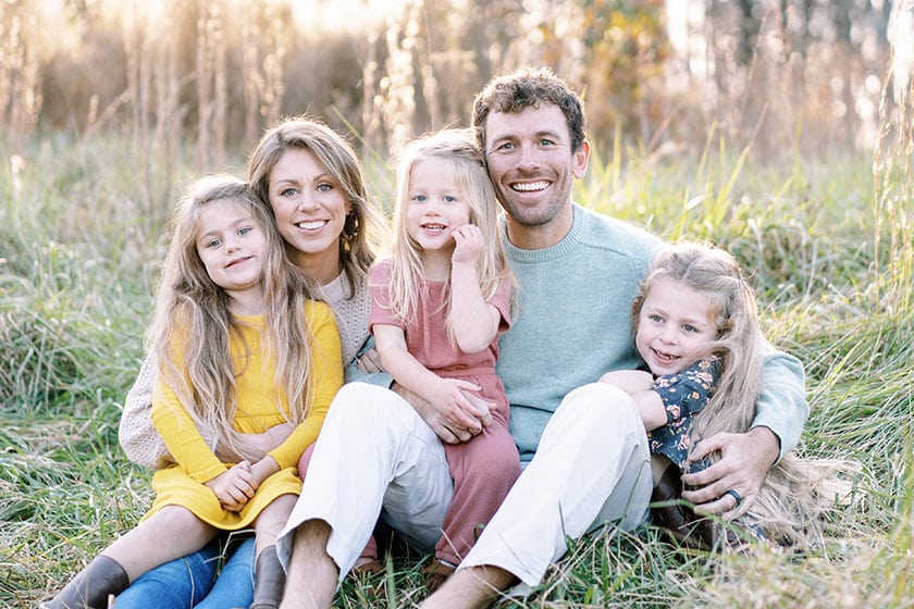 three children sitting with their parents in the grass