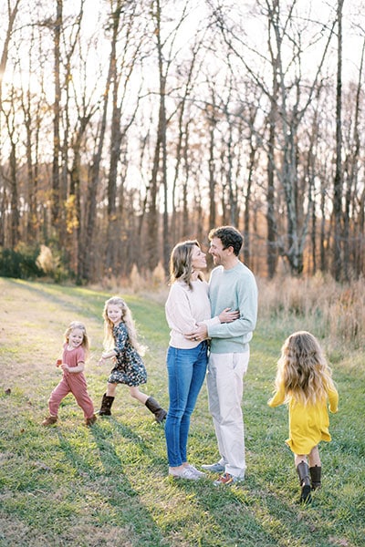 parents hugging with three children running around them