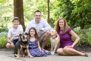 family photo of mom, dad, son, and daughter sitting with their two dogs in a park