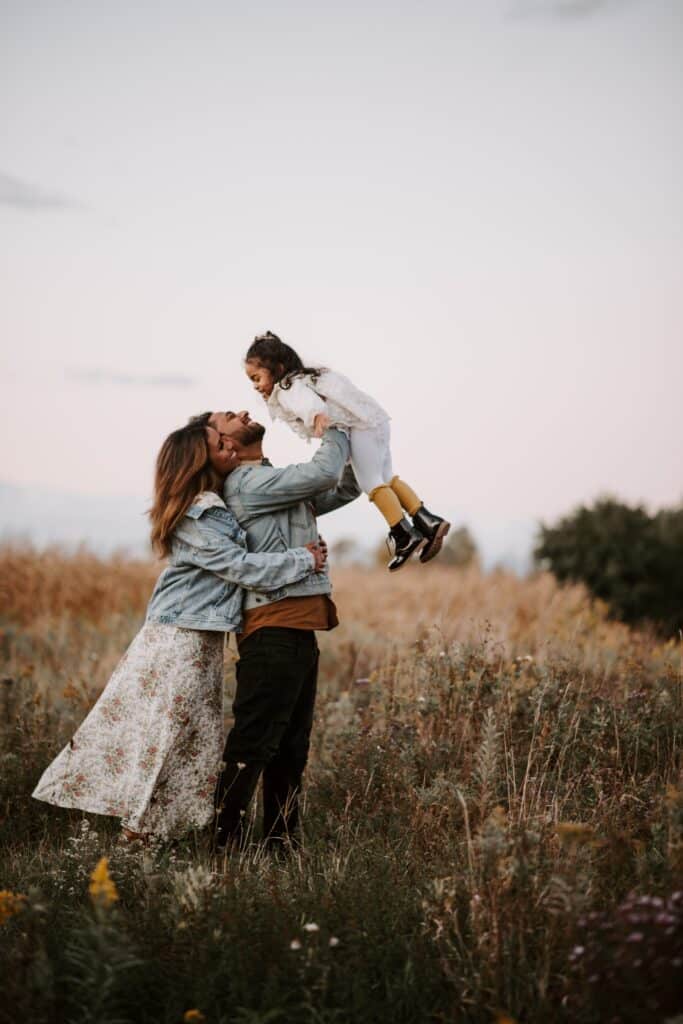 father lifting child in the air while mother hugs him from behind