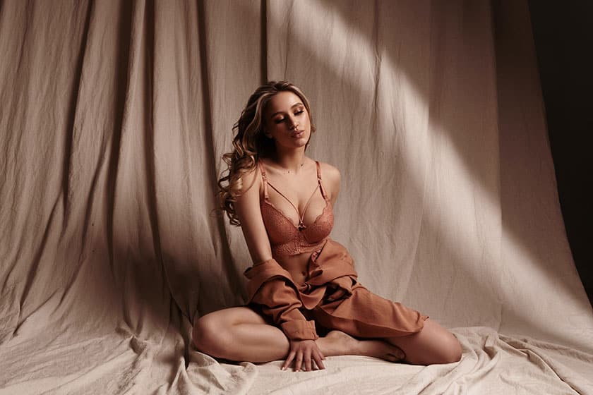 woman posing in lingerie seated, with both legs bent at the knee and folded to her left side.