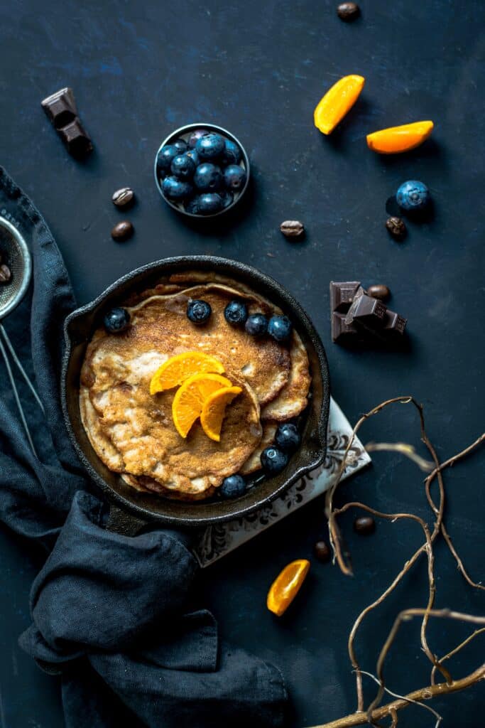 pancakes with blueberries and orange slices on a dark surface