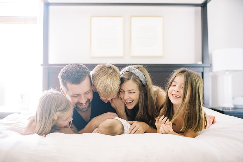 children and parents cuddled on bed with newborn baby