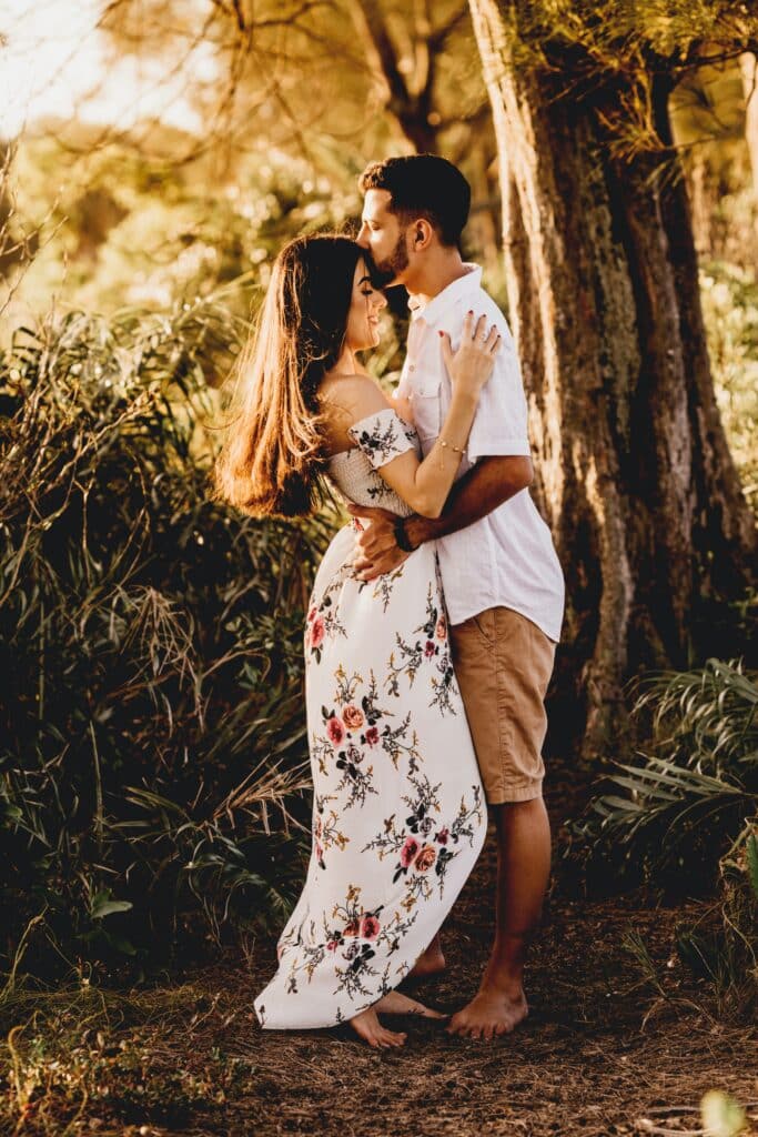 man and woman facing and holding each other while he kisses her forehead