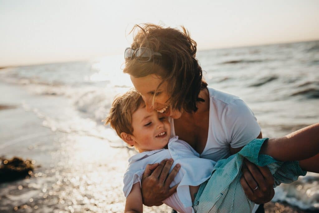 mother carrying son over waves at the beach