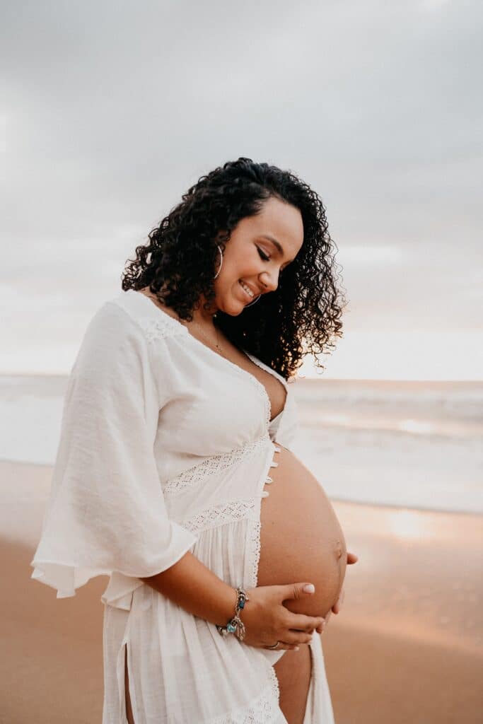 mother in white dress maternity session at the beach