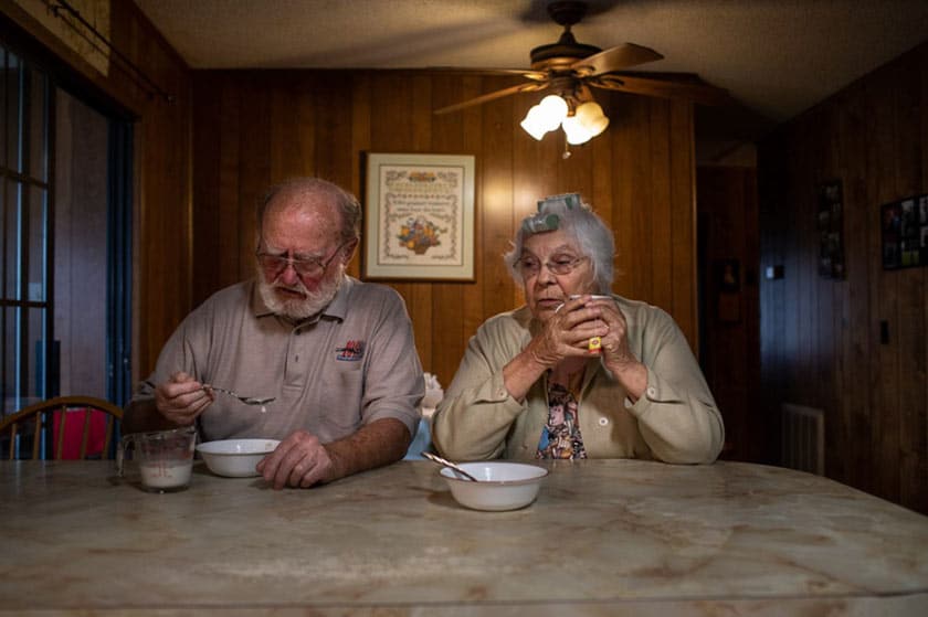 an elderly couple sitting beside one another at the table, eating a meal