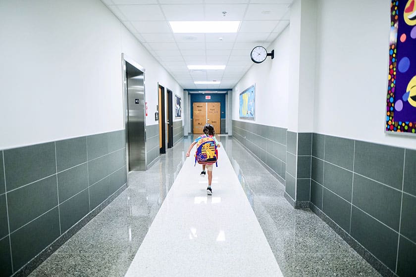 child with backpack in empty school hallway