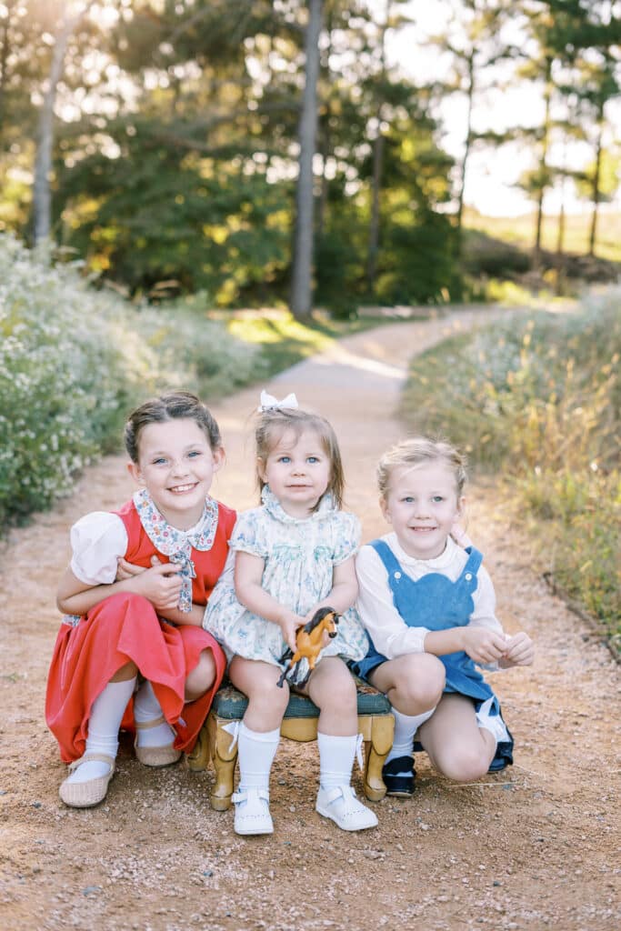 three young sisters wearing dresses sitting in gravel path