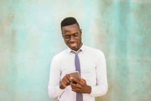 black man with his back to a textured aqua wall while holding and looking at his phone