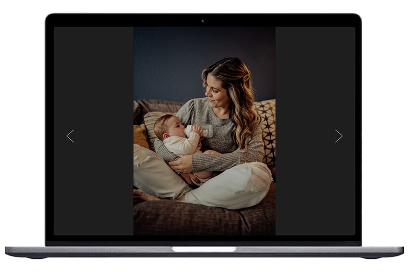 Member spotlight of Valerie Marie photography. Image of mother smiling while holding and feeding child seated cross-legged on a couch.