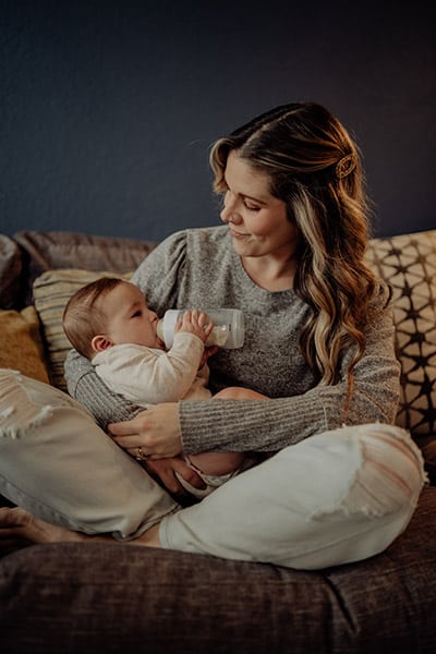 mother smiling while holding and feeding her baby