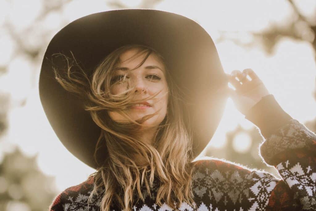 woman looking at camera and touching her hat at golden hour